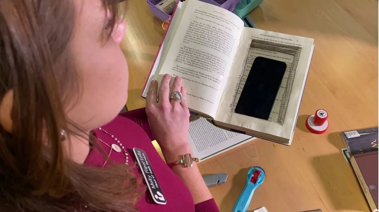 Librarian holds a book with a hole cut of the inner pages to store a cell phone.