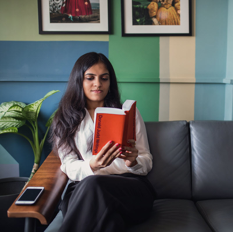 Person reading book indoors, next to smartphone